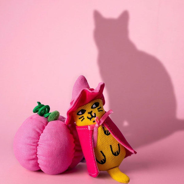 Peluche Halloween à la cataire Ziggy en sorcière, près de citrouilles roses et d’une silhouette de chat